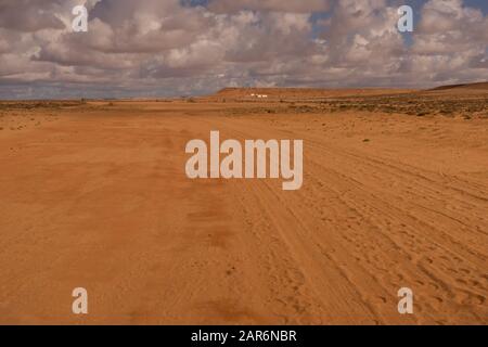 un percorso verso l'orizzonte nel deserto, alcune case in lontananza Foto Stock