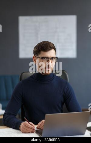 Giovane uomo d'affari che lavora in ufficio con un computer portatile. Ritratto d'affari di bell'uomo portante gli occhiali seduti sul posto di lavoro. Sicuro Foto Stock
