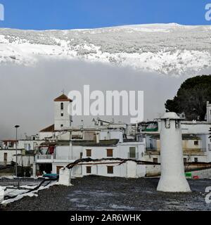 Una vista della chiesa nel villaggio di Capileira in inverno, con montagne innevate sullo sfondo. Foto Stock