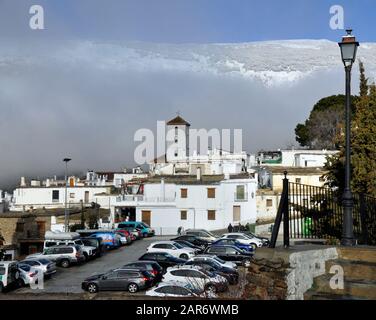 Una vista della chiesa nel villaggio di Capileira in inverno, con montagne innevate sullo sfondo. Foto Stock