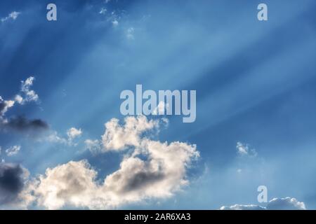 Raggi del sole che si infrangono attraverso le nuvole contro un cielo blu brillante, per l'uso come sfondo astratto e texture. Foto Stock