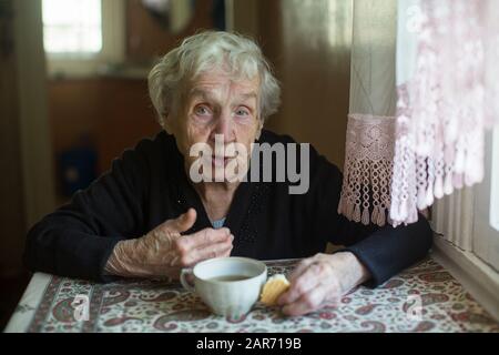 Donna anziana che beve tè con biscotti a casa. Foto Stock