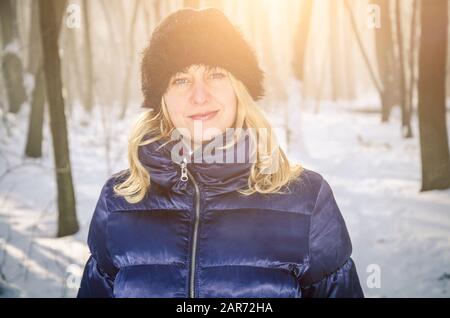 Ritratto di una donna bionda in giacca blu e cappellino in pelliccia nella foresta invernale innevata Foto Stock