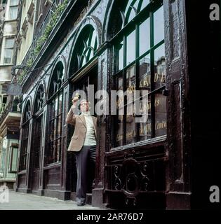 London 1970s, MAN esamina un bicchiere di vino sherry al di fuori del negozio di vendita di vini Berry Bros. & Rudd, St James Street, Inghilterra, Regno Unito, GB, Gran Bretagna, Foto Stock