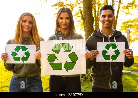 Giovani volontari che detengono il simbolo di riciclaggio placard all'aperto Foto Stock