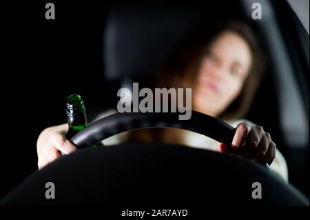 La ragazza si appoggiò sul sedile del conducente e le tiene le mani sul volante, in una delle sue mani ha una bottiglia di alcol Foto Stock