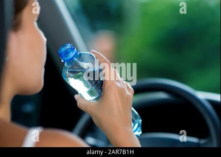 giovane donna guida un'auto e sta per bere acqua da una bottiglia Foto Stock