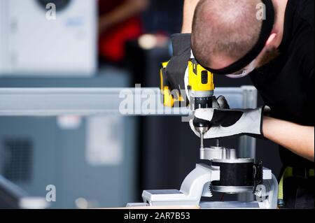 Il lavoratore in una T-shirt nera stringe un bullone in un pezzo di ricambio serrato in una morsa Foto Stock