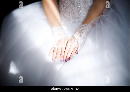 La sposa in un abito da sposa mettere le mani sulle ginocchia ed è illuminata da un raggio di luce dalla finestra Foto Stock