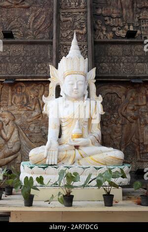Una statua buddista di Bodhisattva bianca e dorata contro un gelo di legno intricato, Tempio di Ganagaramaya, Colombo, Sri Lanka Foto Stock
