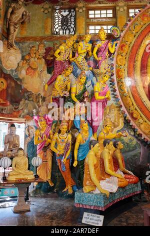 Figure dai colori vivaci che fiancheggiano una grande statua del buddha seduto nel Tempio di Gangaramaya, Colombo, Sri Lanka Foto Stock