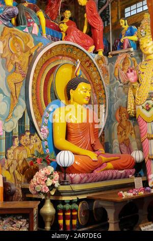 Figure dai colori vivaci che fiancheggiano una grande statua del buddha seduto nel Tempio di Gangaramaya, Colombo, Sri Lanka Foto Stock