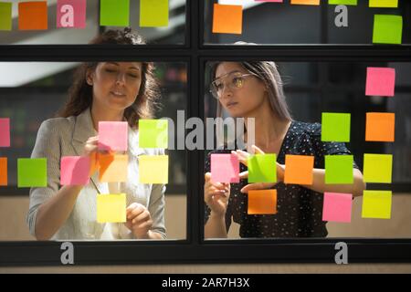 Dipendenti multietnici di sesso femminile brainstorming utilizzando note adesive Foto Stock