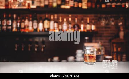 Bicchiere di whisky con supporti di ghiaccio sul bancone del bar, fondo marrone scuro Foto Stock