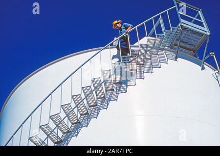 Un tecnico di gas naturale liquefatto che cammina lungo le scale di un serbatoio di stoccaggio GNL Foto Stock