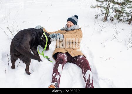 Gioioso ragazzo in winterwear divertirsi giocando con nero Retriever nella neve Foto Stock