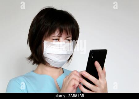 Donna in maschera medica con smartphone, telefono cellulare in primo piano in mani femminili. Concetto di malattia, febbre, raffreddore e influenza, sintomi di coronavirus Foto Stock