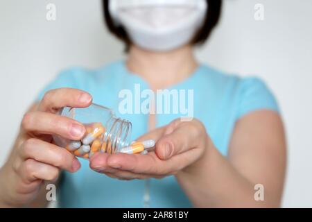 Donna con pillole, medico in maschera medica con flacone di capsule. Concetto di dose di farmaci, vitamine, coronavirus e trattamento influenzale Foto Stock