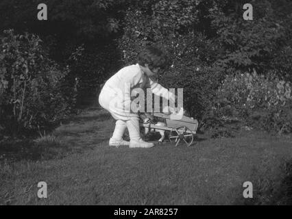 Anni '1920, storica, una bambina all'aperto in un giardino che gioca con la sua bambola seduta in un giocattolo di legno cavallo e carrello, Inghilterra, Regno Unito. Foto Stock