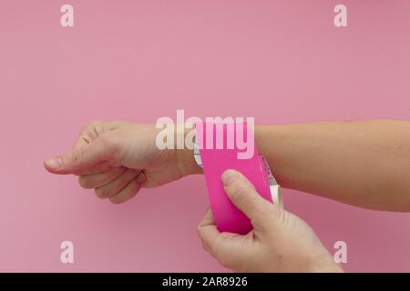 Applicazione di un nastro in kinesio isolato a mano su sfondo rosa. Nastro fisioterapico per dolori al polso, dolori e tensione. Nastro terapeutico elastico. Adesivo Foto Stock