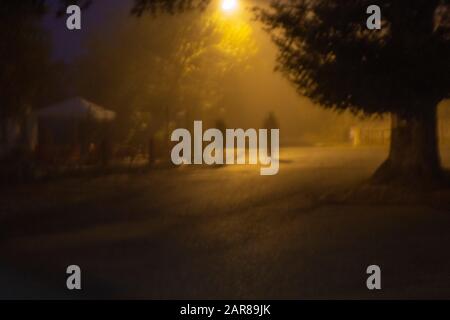 Indistinte figure sfocate che camminano di notte illuminate da lampione giallo Foto Stock