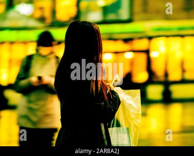 Una figura offuscata e irriconoscibile di una giovane ragazza che si scagliava giù per strada con un cappotto scuro e un telefono cellulare nelle sue mani. Silhouette stilizzata di un giovane moderno Foto Stock