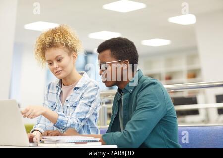 Ritratto di due studenti che puntano sullo schermo del laptop mentre si lavora su progetto in biblioteca universitaria, copia spazio Foto Stock