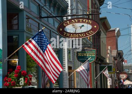 Clayton, NY, USA - Luglio, 2019: Building Shop Facade su James St durante la stagione estiva, bandiere americane e cartelli in legno di ferro Foto Stock