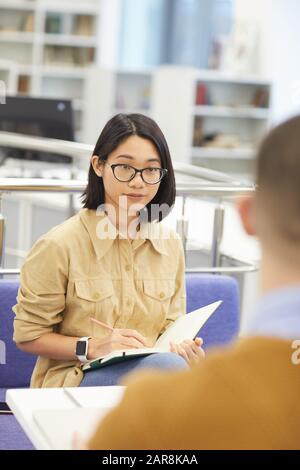 Ritratto di ragazza asiatica indossare occhiali mentre si lavora su progetto di gruppo con partner di studio in biblioteca Foto Stock