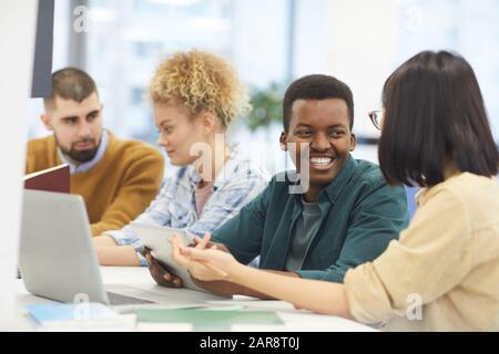 Gruppo multietnico di studenti che studiano in biblioteca universitaria, concentrarsi su uomo afro-americano sorridente al partner Foto Stock