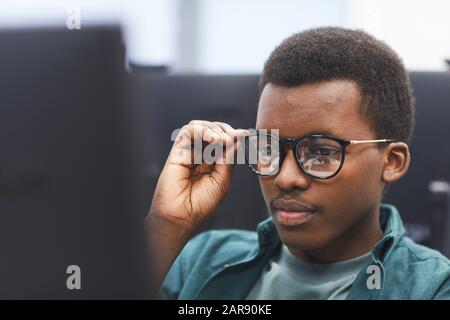 Ritratto ad alto angolo di uomo africano-americano che regola gli occhiali mentre usando il calcolatore nella classe della biblioteca dell'università, spazio della copia Foto Stock