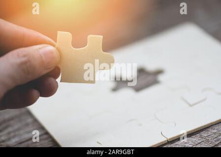 Uomo d'affari che tiene il puzzle / primo piano di pezzi di puzzle per unire e provare a collegare il concetto di partnership di affari Foto Stock