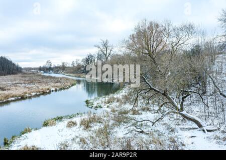 paesaggio invernale con piccolo fiume sotto cielo nuvoloso. alberi e riva del fiume coperta di neve Foto Stock