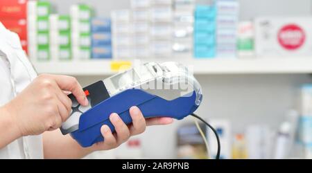 Fare acquisti, Pagare con una carta di credito e utilizzando un terminale su molti scaffali medicinali in background farmacia. Foto Stock