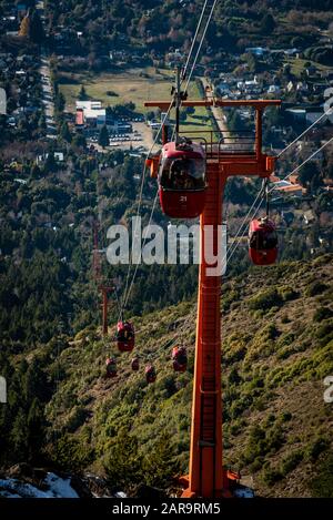 Vista prospettica delle funivie rosse che trasportano i passeggeri sulla cima delle montagne viste sullo sfondo. Foto Stock