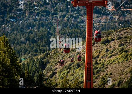 Vista prospettica delle funivie rosse che trasportano i passeggeri sulla cima delle montagne viste sullo sfondo. Foto Stock