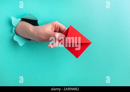 La mano si distende una busta rossa dal foro sullo sfondo turchese. Concetto di San Valentino Foto Stock