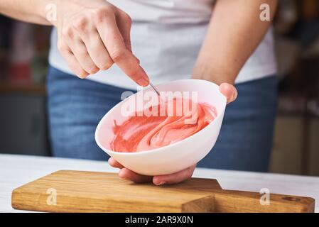 Donna colore rosso sbattere la panna per decorare i cookie in un recipiente da cucina, primo piano Foto Stock