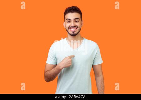 Questo è me! Ritratto di felice uomo brunetta soddisfatto con barba in t-shirt bianca che punta a se stesso, guardando la macchina fotografica con sorriso fiero e boastful. Foto Stock