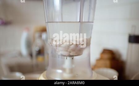 Frullatore e mandorle imbevuto di acqua. Facendo sano latte vegano. Foto Stock