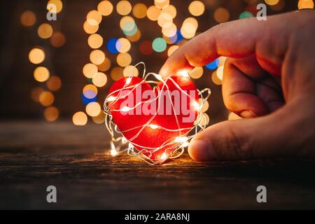 Tenendo una forma di cuore rosso coperto con luci a LED su sfondo legno e bokeh luci. San Valentino e concetto romantico Foto Stock