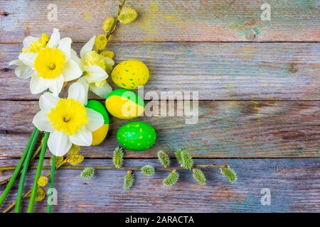 Composizione pasquale di daffodil fiore di ramoscelli salici fioriti e uova di Pasqua con un motivo di giallo e verde su uno sfondo retrò di legno con c Foto Stock