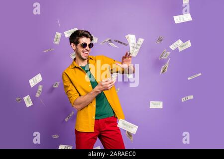 Foto di allegro bianco eccitato uomo alla moda gettando denaro via mostrando il suo più ricco sorridente dentifricio in pantaloni rossi isolato viola colore sfondo Foto Stock