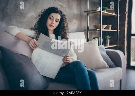 Ritratto di lei bella affascinante bella cute messa a fuoco pacifica capelli ondulati ragazza seduta su divano lettura digest notizie a industriale moderno Foto Stock