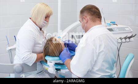 Medico dentista considera i denti di una giovane e bella ragazza paziente. La ragazza alla reception presso il dentista. Medico dentista considera dente Foto Stock
