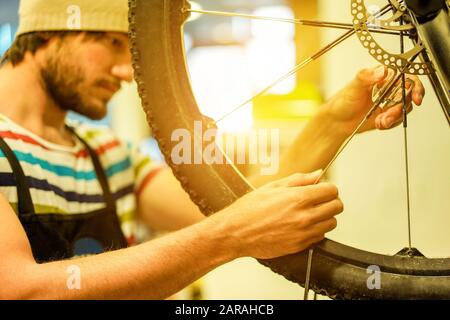 Elegante meccanico bearded della bicicletta che fa il suo lavoro professionale in officina - giovane uomo trendy che controlla la ruota della razza - concetto di riparazione delle bici - fuoco sopra Foto Stock