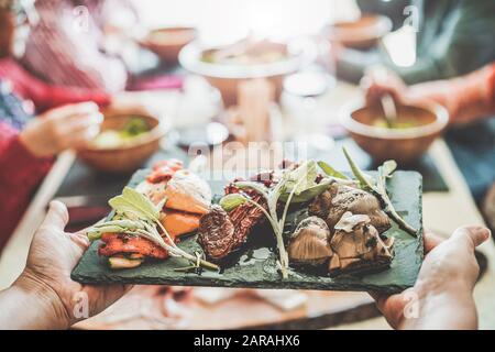 Chef donna che serve pomodori secchi, carciofi cotti, peperoni all'interno di un ristorante gastronomico vegetariano - Happy Senior persone che hanno pranzo e bere Foto Stock