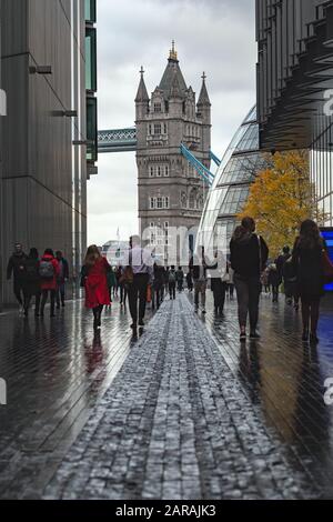 Londra, Inghilterra - novembre 2019. Una torre del famoso Tower Bridge e City Hall vista da Più London Riverside. Persone che camminano su strade bagnate tra Foto Stock