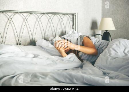 La ragazza al mattino a letto usa un cellulare. Tecnologia moderna nella vita di tutti i giorni. Foto Stock