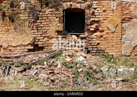 Finestra rotta montata su mattoni rossi muro di rovine di vecchio legno distrutto e mattoni casa suburbana famiglia mista con piccole piante nella parte vecchia della città Foto Stock